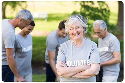A senior woman stands smiling with a group of volunteers wearing volunteer t-shirts